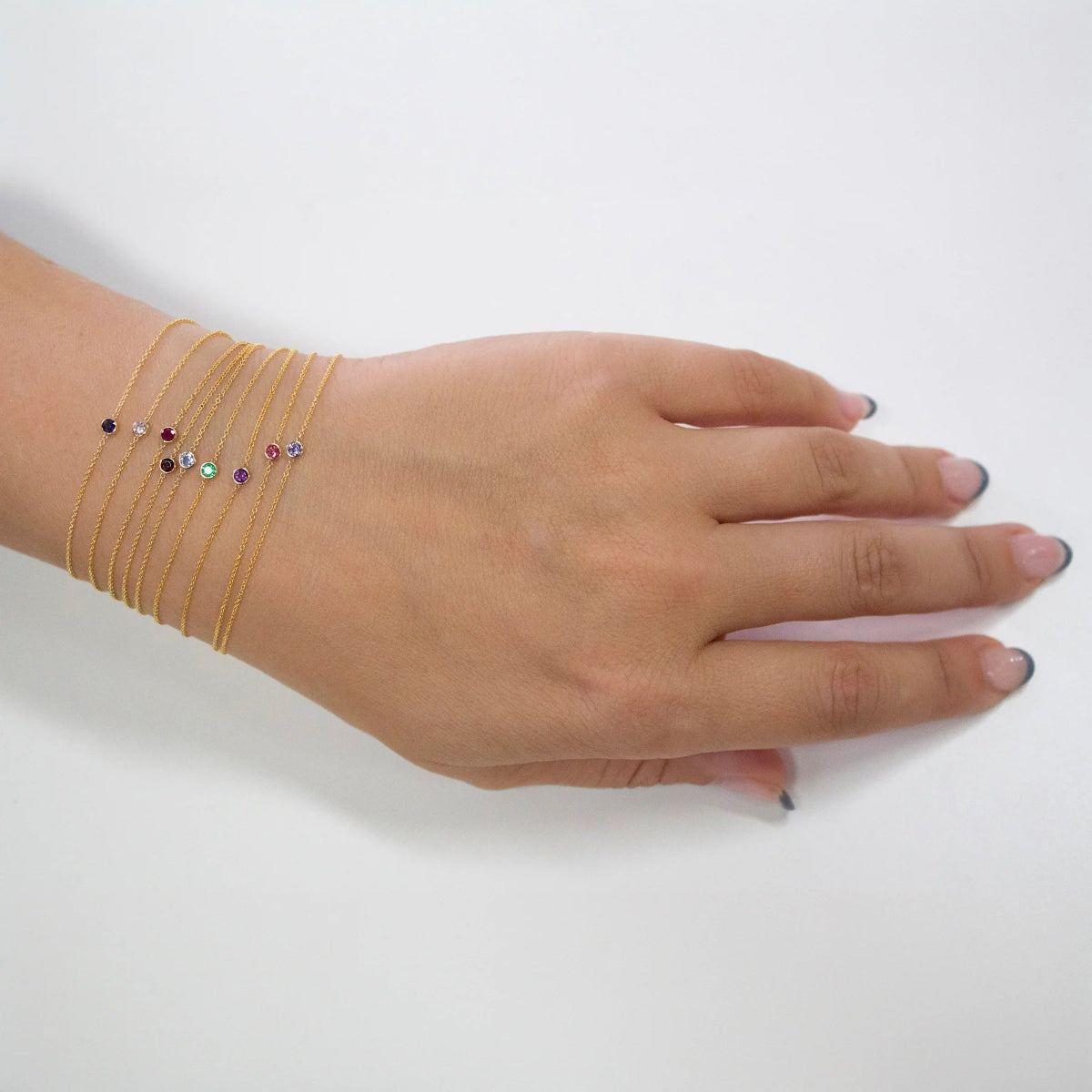 Hand wearing multiple thin gold bracelets with small gemstones on a white background