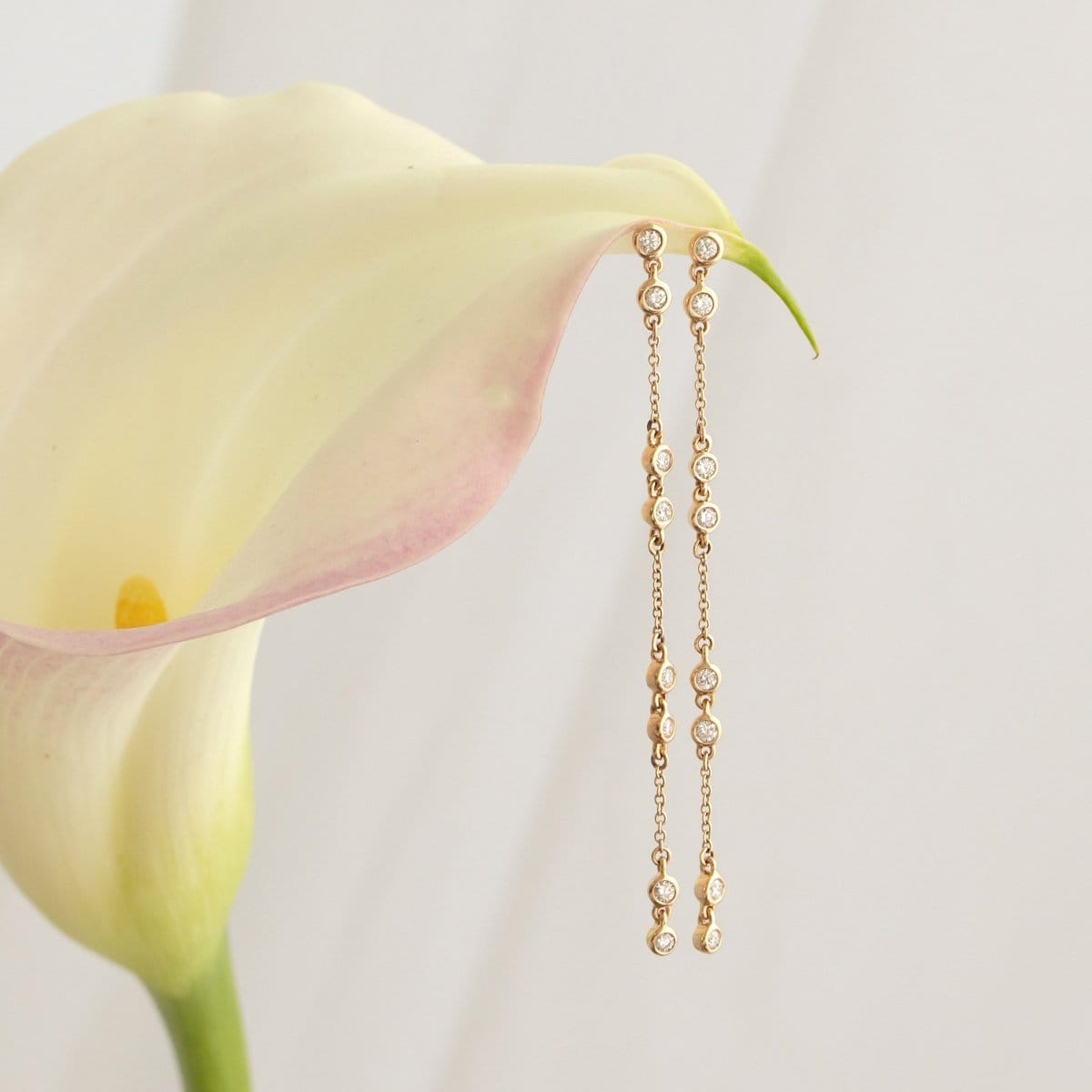 A pair of Stardust Earrings in yellow gold on a lily flower against a white background. 