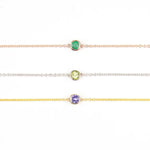 Three 14K Gold Asymmetrical Birthstone Necklaces - Emerald (May) in rose gold, Peridot (August) in white gold and Tanzanite (December) in yellow gold on a white background. 