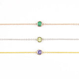 Three 14K Gold Asymmetrical Birthstone Necklaces - Emerald (May) in rose gold, Peridot (August) in white gold and Tanzanite (December) in yellow gold on a white background. 