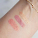 Three swatches of makeup colours on a person's arm with a gold bracelet with a J letter charm. 