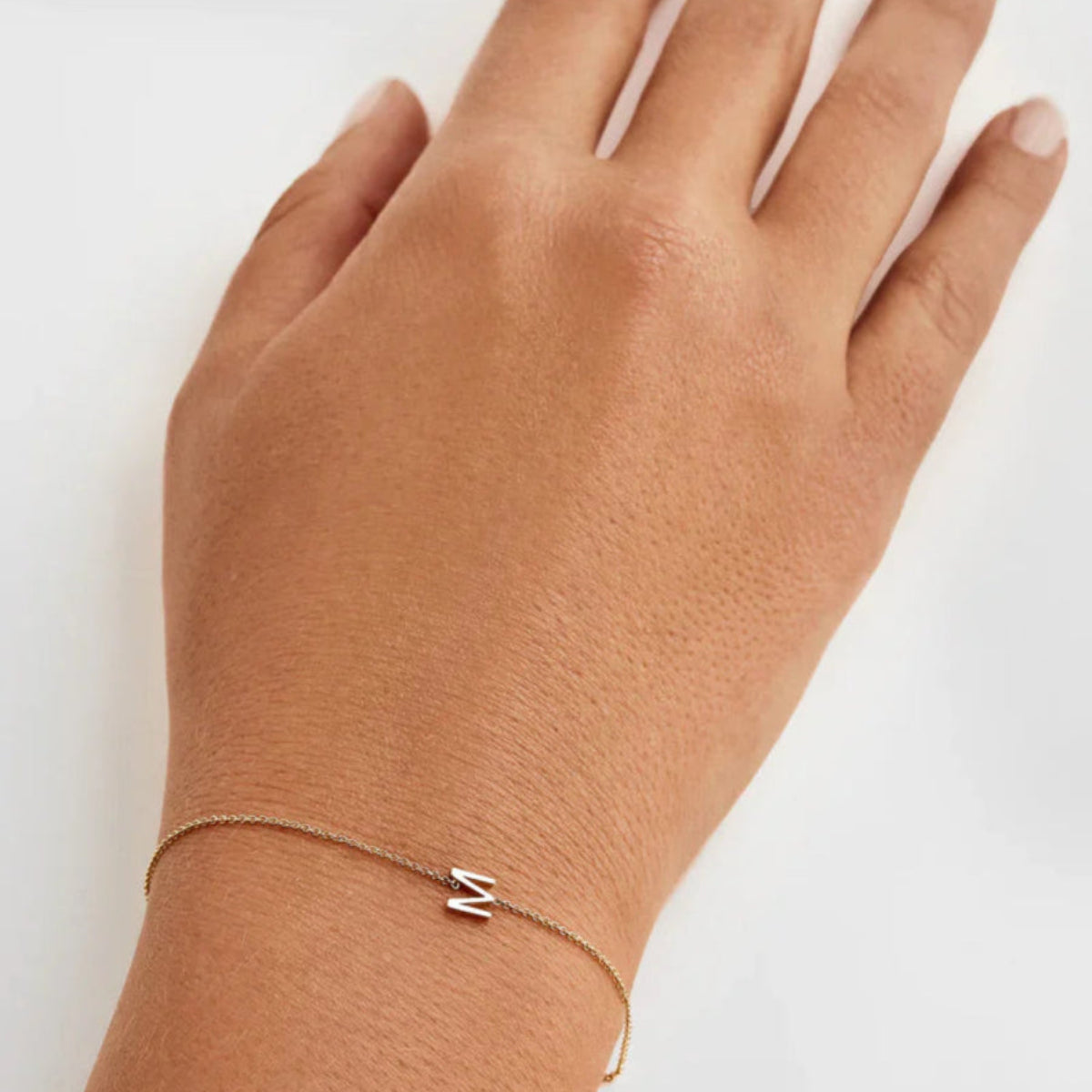 A hand wearing a Custom Gold Bracelet - 1 Letter with the letter M on a white background. 