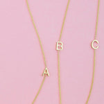 Three gold necklaces with single letter charms A, B and C on a pink background. 