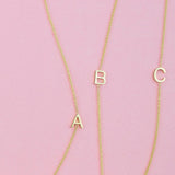 Three gold necklaces with single letter charms A, B and C on a pink background. 