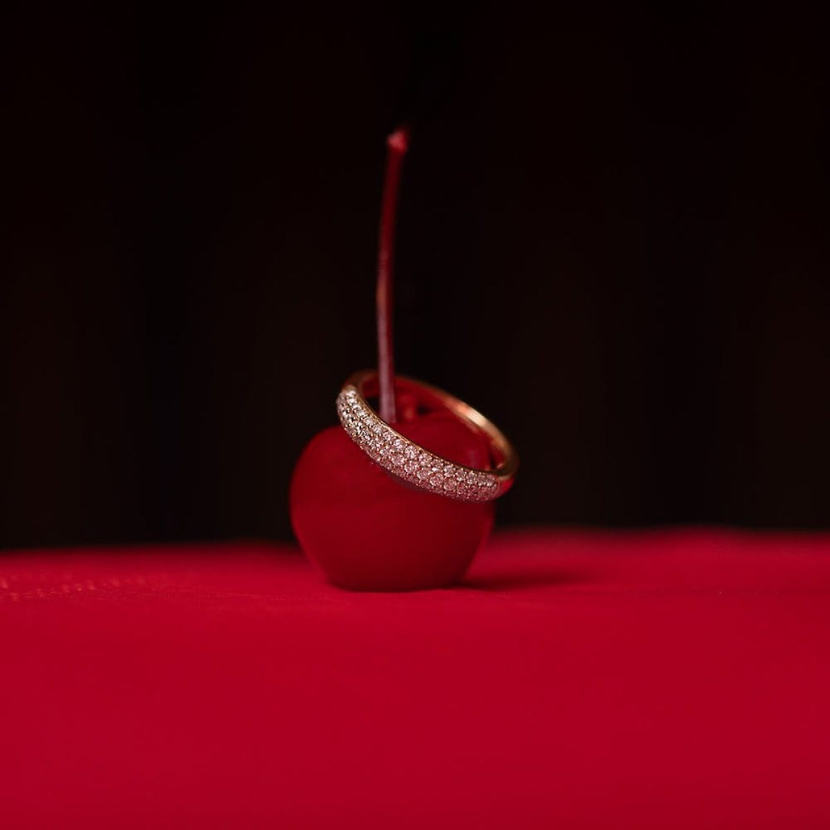 A Cosmo Ring on top of a cherry against a red and black background. 