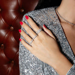 A hand wearing several Cosmo Rings with red nails resting on a sequenced top, against a brown leather background. 