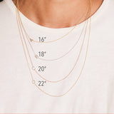Four gold initial necklaces around a women's neck shown in different lengths.