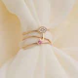 Three gold rings, including a yellow gold Pavé Petal Ring, a rose gold J Letter Ring, and a rose gold Birthstone Ring on a cream fabric background.