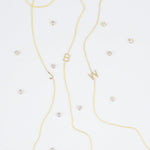 Three gold necklaces with single letter charms, being J, B and W, featuring multiple little gemstones on a white background.