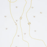 Three gold necklaces with single letter charms, being J, B and W, featuring multiple little gemstones on a white background.