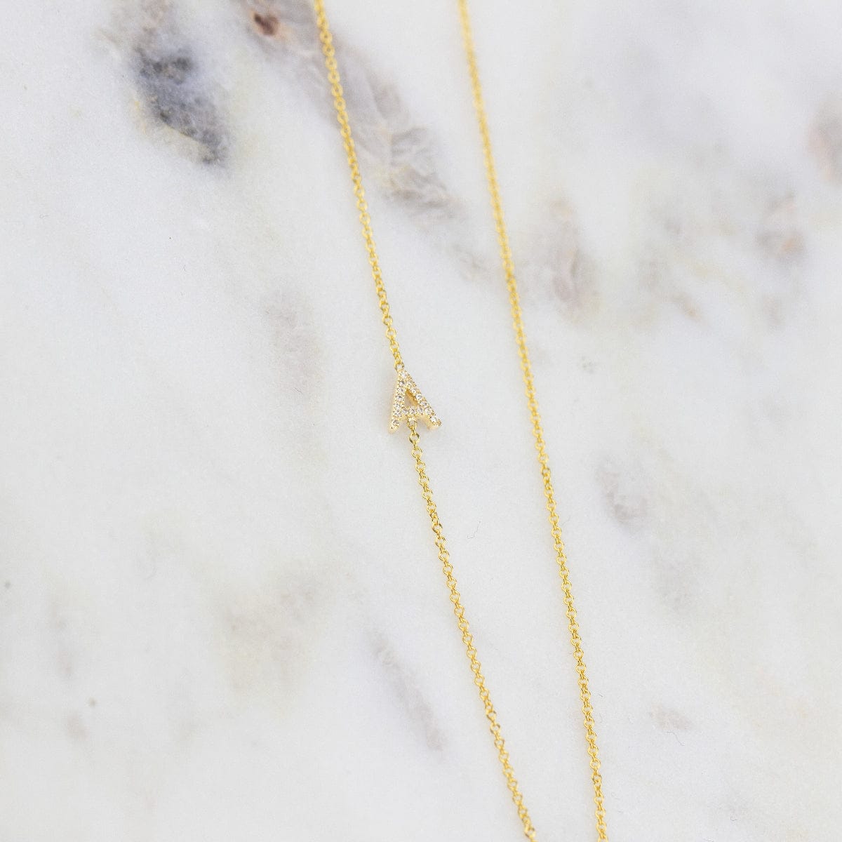 A gold necklace with a pave letter A charm  on a marble background.