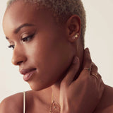 Woman wearing gold single letter and heart earrings, rings and necklaces with a neutral background. 