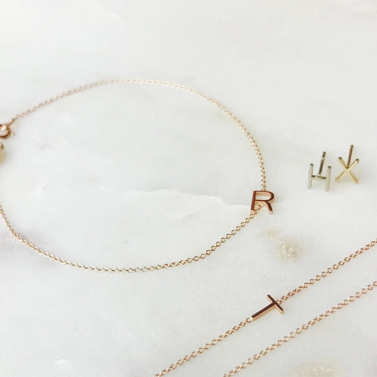 Single letter jewellery including a necklace, bracelet and earrings on a white background.