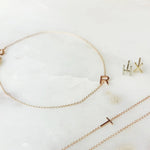 Single letter jewellery including a necklace, bracelet and earrings on a white background.
