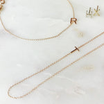 A necklace, bracelet and two stud earrings, each with its own letter charm – R, T, H, and X against an off white marble background. 