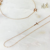 A necklace, bracelet and two stud earrings, each with its own letter charm – R, T, H, and X against an off white marble background. 