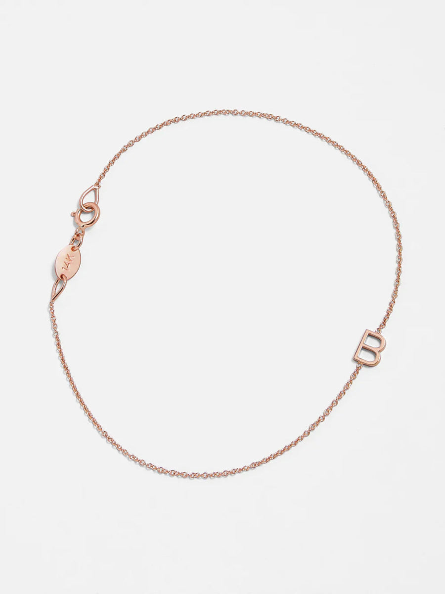 A rose gold bracelet with an B letter charm on a white background. 