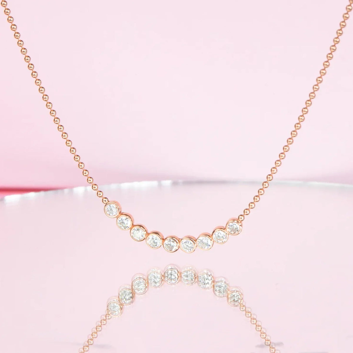 A Diamond Arc Layering Necklace in yellow gold against a light pink background. 