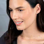 A Heartfelt Stud and Custom Gold Necklace - 3 Letters in rose gold worn by a brunette woman against a light grey background. 