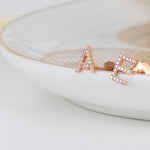 Two rose gold pave single letter studs A and E in a white bowl.