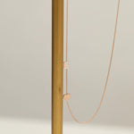 A Monogram Necklace with Heart Rose Gold and a letter E charm next to a brown stick against a light grey background. 