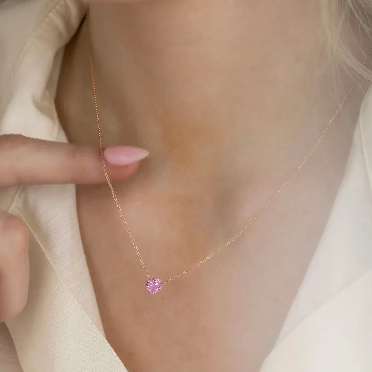 Close-up of a neck wearing The Sweetheart Necklace - Pink Sapphire in rose gold with a cream shirt.