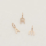 A Petite Letter Charm in m, a Gold Letter Charm in A and a Pavé Letter Charm in R, all in rose gold, against a white textured background. 