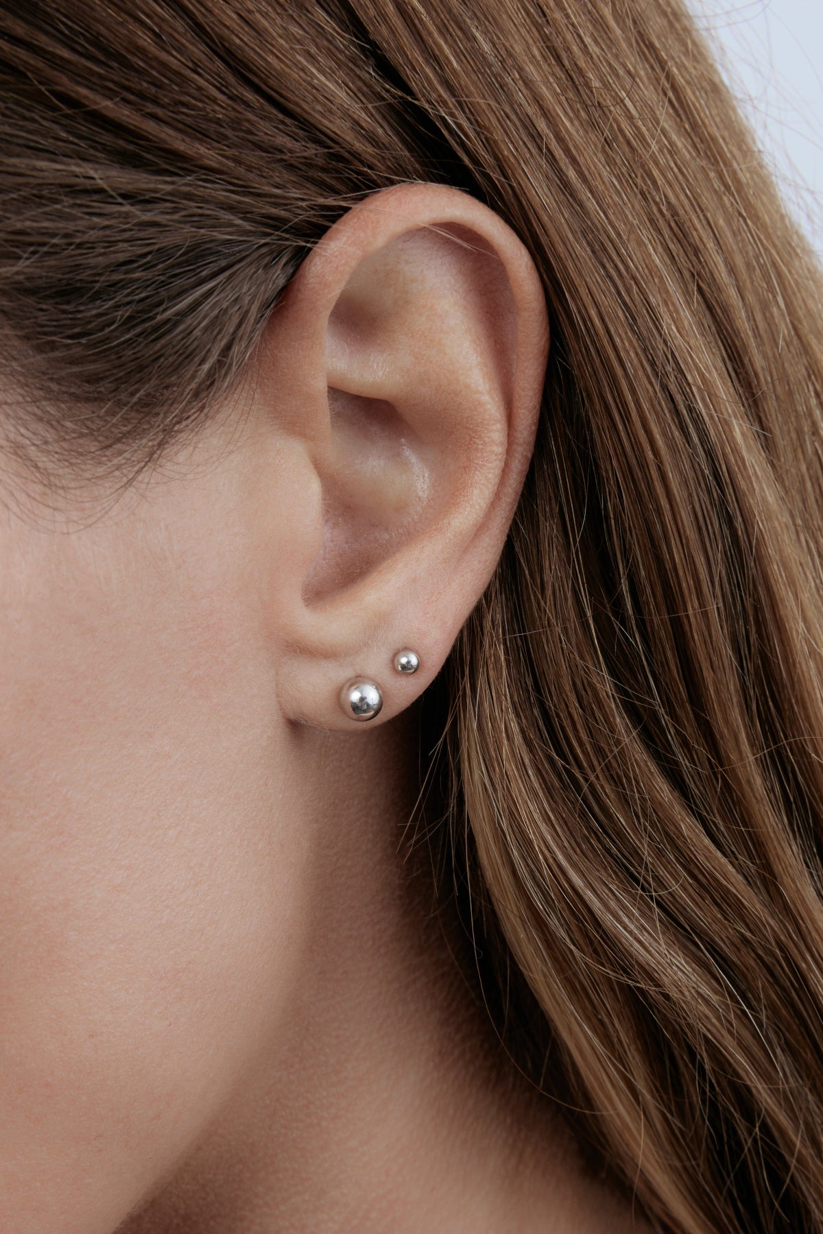 Close-up of a white gold Mini Preppy Post and Preppy Post in a brunette woman's ear. 