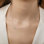 A close-up of a woman's neck wearing two white gold 14k Gold Asymmetrical Charm Necklaces in - Heart and Pavé Heart, styled in a white jacket. 
