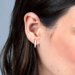 Close-up of a Horizon Stud in white gold worn on a brunette woman's ear against a light grey/blue background. 