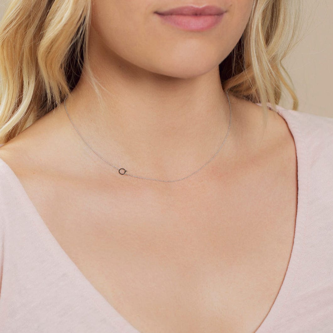 A close-up of a woman's neck wearing a white gold necklace with a letter Q charm.
