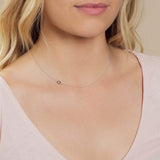 A close-up of a woman's neck wearing a white gold necklace with a letter Q charm.