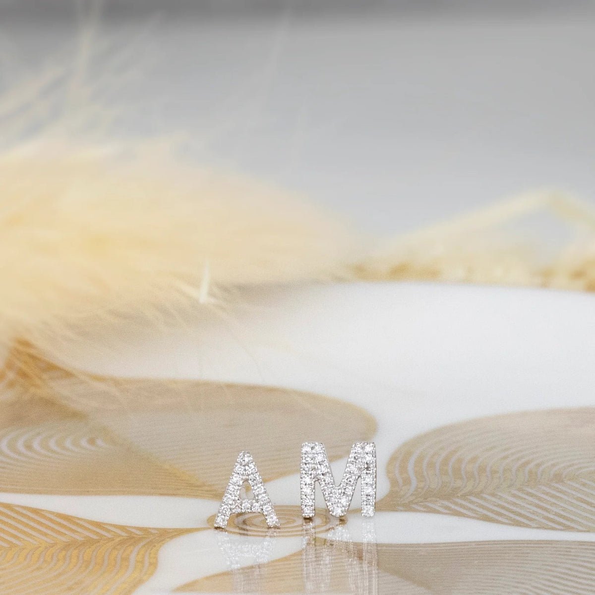White gold pave letter stud earrings A and M on a white and gold surface. 