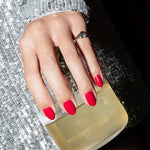 A woman's hand wearing a white gold Pinky Promise Ring with red nails, in a silver dress holding a drink. 