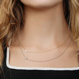 A close-up of a woman's neck wearing two 14k Gold Asymmetrical Charm Necklaces (one star in yellow gold and one pavé star in white gold), styled with a black and white top.