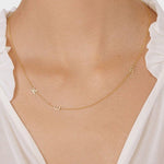 A close-up of a woman’s neck wearing a Custom Gold Necklace in yellow gold with three letter charms, a K and an E on the left side and a B on the right side, and a white blouse.