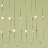 Four Custom Gold Necklaces in yellow gold, three with five different charms and one with six, laid against a light green background.