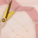 A Custom Gold Necklace in yellow gold with 6 charms (two Cs, S, E, a birthstone and a heart) on pink fabric with a pair of gold scissors.