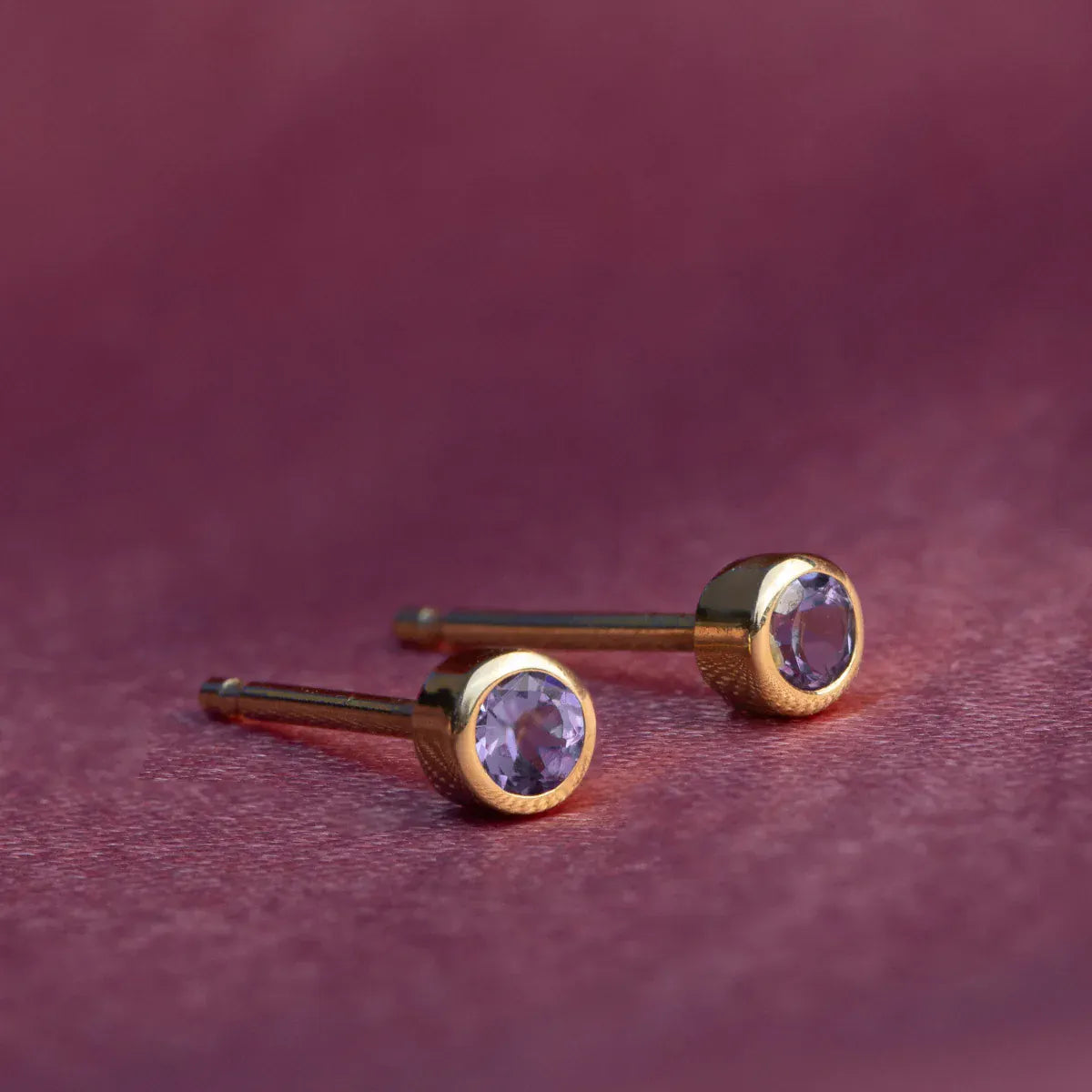 A pair of Birthstone Stud - Amethyst (February) in yellow gold against a dark purple background. 