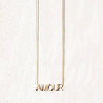 An AMOUR Necklace in yellow gold on a cable chain on an off-white background. 