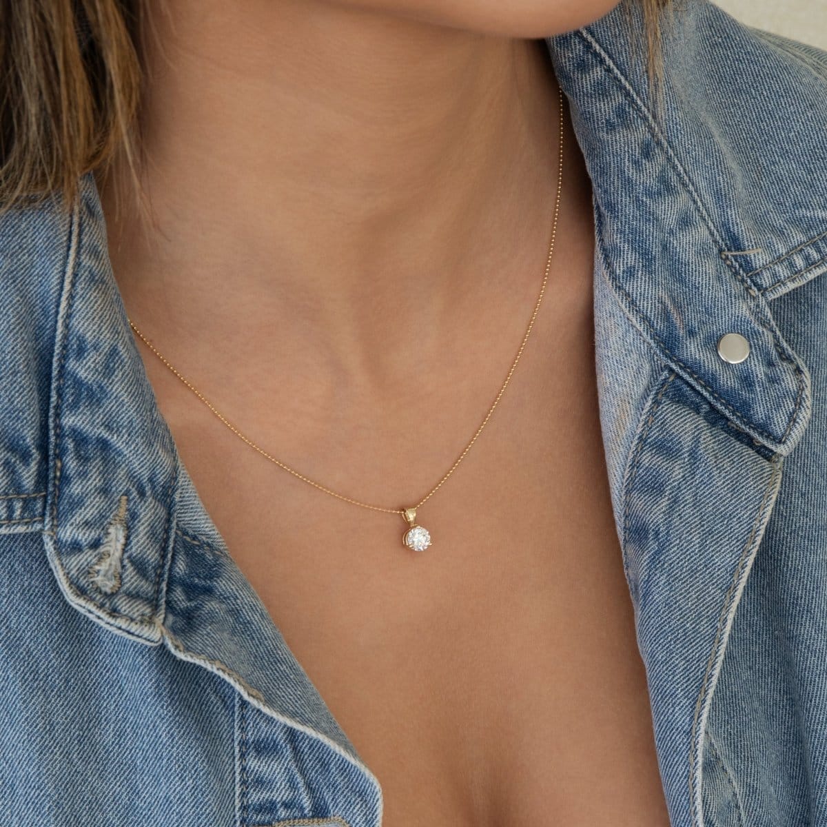 Close-up of a woman's neck wearing a yellow gold Classic Bead Chain with a Diamond Pendant and a denim top. 