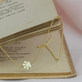 A 4k Gold Asymmetrical Charm Necklace - Paw with a beaded chain wrapped around the corner of a book, against a light background.