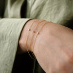 A close-up of a wrist wearing three Birthstone Bracelets (two pearls and one pink tourmaline), styled with a sage green shirt. 