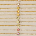 Twelve yellow gold 14K Gold Asymmetrical Birthstone Necklaces - three Diamond (April), three Citrine (November), three Peridot (August), one Garnet (January) and two Pink Tourmaline (October) laid against a neutral background. 