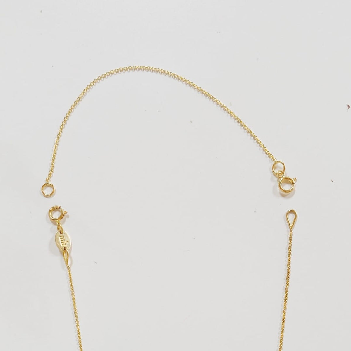 A yellow gold chain extender shown on top of a partially visible yellow gold cable-chain necklace on a light grey background.