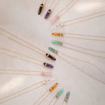 Several Retreat Necklaces in various colours on a cream soft-textured background.