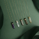 Five The Retreat Necklaces (Healing, Clarity, Protection, Courage and Happiness) laid against a dark green background.