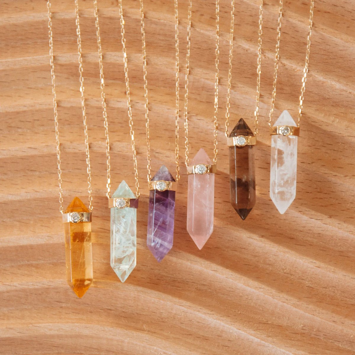 Six Retreat Necklaces (Happiness, In Flow, Healing, Love, Courage and Clarity) on a wooden background. 