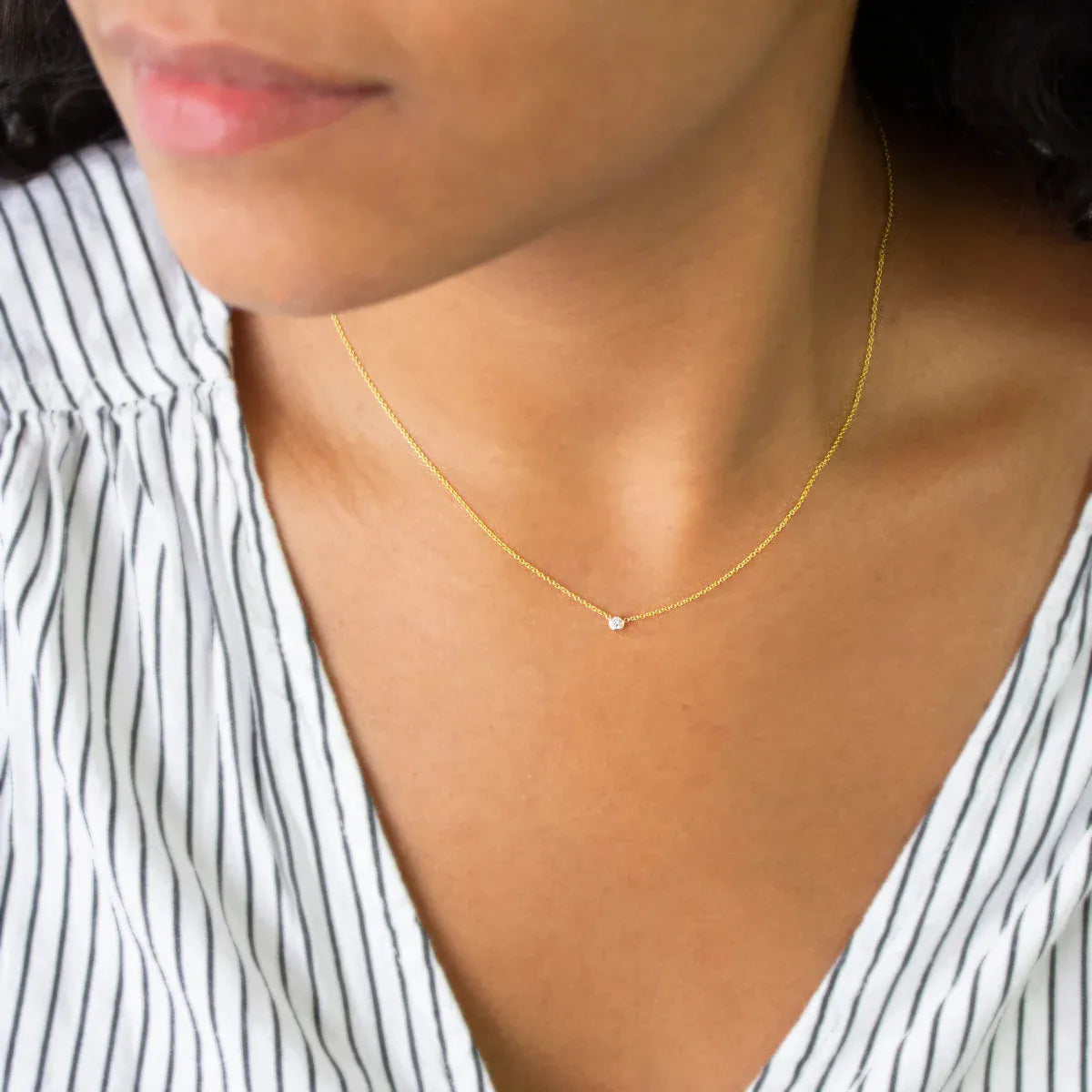 A close-up of a woman's neck wearing a yellow gold Diamond Layering Necklace, styled in a black and white stripe top. 