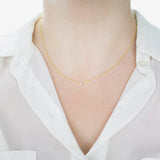 A close-up of a woman's neck wearing a yellow gold Diamond Layering Necklace, styled in a white shirt. 
